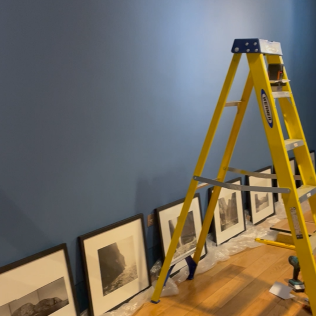 A ladder near a wall, with some framed photographs on the floor.