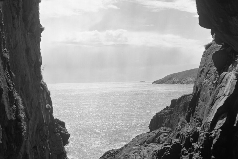 Black and white photograph of the sea seen through the cliffs.